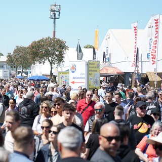 Viele Besucher auf einer Straße beim Mannheimer Maimarkt. Die Besucher laufen an einem sonnigen Maimarkttag die Straße zwischen den Zelten entlang. 