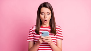Eine Frau schaut überrascht auf ihr Smartphone.