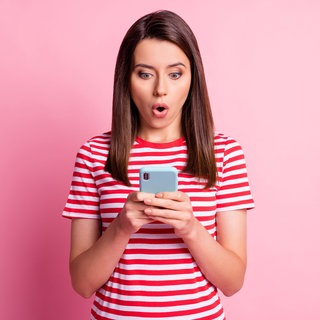 Eine Frau schaut überrascht auf ihr Smartphone.