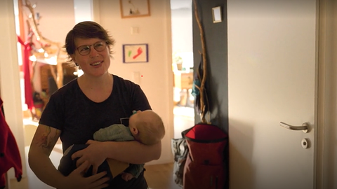 Eine Frau mit Baby auf dem Arm öffnet ihre Wohnungstür