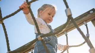 Ein kleines Mädchen klettert auf einem Spielplatz.