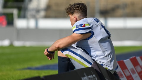 Stuttgart Surge Spieler Noah Bomba sitzt in Football-Montur auf einer Werbebande