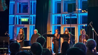 Fünf Frauen und Männer in Konzertgarderobe beim Schlussapplaus auf der Bühne