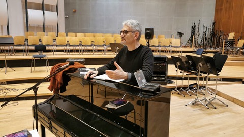 Mann mit schwarzer Brille lehnt an schwarzem Klavier