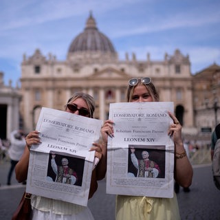 Mackenzie Magas und Kaylee Mellentine aus Missouri posieren für ein Foto mit einer Zeitung, die den neuen Papst Leo XIV. auf der Titelseite zeigt, vor dem Petersdom im Vatikan.