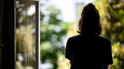 Eine Frau steht in ihrer Wohnung an einem Fenster