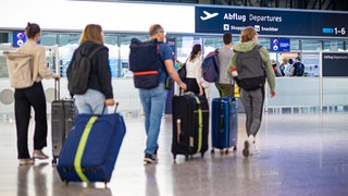 Personengruppe mit Rollkoffern auf dem Weg zum Flugschalter im Flughafen