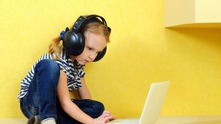Mädchen sitzt mit Kopfhörern vor einem Laptop.