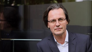 Prof. Bernhard Pörksen blickt in die Kamera. Warum können die Menschen heute offenbar nicht mehr empatisch miteinander reden, sich zuhören und gegenseitig verstehen? Das erforscht der Tübinger Medienwissenschaftler Prof. Bernhard Pörksen.  In SWR1 Leute sprechen wir mit ihm über sein Buch "Zuhören: Die Kunst sich der Welt zu öffnen".