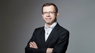 Sönke Iwersen, Investigativ-Reporter des Handelsblatt, steht im Anzug und mit verschränkten Armen da.