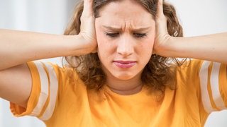 Eine junge Frau hält sich die Ohren zu mit schmerzverzerrtem Gesicht. Hilfe bei chronischem Tinnitus oder Schwindel und Übungen zur Vagusnerv-Stimulation: HNO-Arzt und Tinnitus-Spezialist Uso Walter gibt in SWR1 Leute Tipps zur Selbsthilfe.