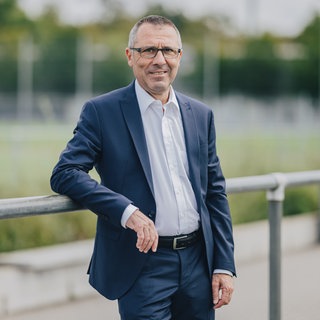 Der ehemalige Präsident der TSG 1899 Hoffenheim schaut freundlich in die Kamera.
