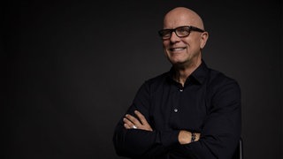 Unternehmer Andreas Buhr lacht mit überschränkten Armen in die Kamera.