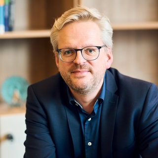 Ökonom Nils Goldschmidt lächelt in die Kamera.  Länder mit hohem sozialen Zusammenhalt sind wirtschaftlich erfolgreicher. Das Weltethos Institut Tübingen will das in konkrete Projekte umsetzen. In SWR1 Leute erläutert Ökonom Nils Goldschmidt die Projekte des Instituts.