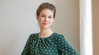 Juristin Carina Amend steht in einem grünen Kleid mit weißten Punkten da.