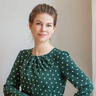 Juristin Carina Amend steht in einem grünen Kleid mit weißten Punkten da.