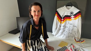 Trikot-Designerin Ina Franzmann sitzt neben einem Deutschland-Trikot mit Unterschriften.