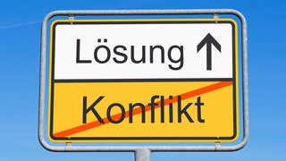 Illustration zum Thema Konflikt-Lösung: Ein Ortsschild zeigt das Wort "Lösung" und das durchgestrichene Wort "Konflikt".  Friedrich Glasl ist Konfliktforscher. Egal, ob Auseinandersetzungen in Beziehung oder Arbeitsplatz oder der Angriffskrieg von Russland auf die Ukraine: er analysiert sie und sucht Lösungen. Wir sprechen mit ihm in SWR1 Leute