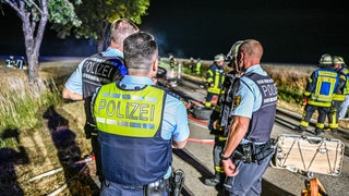 Polizisten bei einem Einsatz mit einem ausgebrannten E-Auto. Symbolbild für psychische Belastungen im Einsatz. 