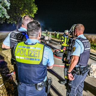 Polizisten bei einem Einsatz mit einem ausgebrannten E-Auto. Symbolbild für psychische Belastungen im Einsatz. 