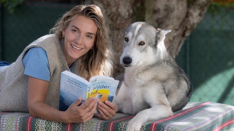 Schlittenhundsportlerin Marina Brutscher liegt bäuchlings mit einem ihrer Huskys auf einer Bank.