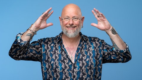 Hypnotiseur und Bühnenkünstler Jan Becker macht eine Pose und lacht in die Kamera.