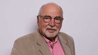 Kreuzfahrtschiff-Seelsorger Albert Matthias Neumann schaut direkt in die Kamera. Zu DDR-Zeiten war er Bassist in der Band von Nina Hagen. Nach seiner Ausreise aus der DDR war er fast 20 Jahre evangelischer Pastor im Hamburger Stadtteil Othmarschen und auch als Seelsorger auf Kreuzfahrtschiffen unterwegs. Darüber unterhalten wir uns mit ihm in SWR1 Leute.