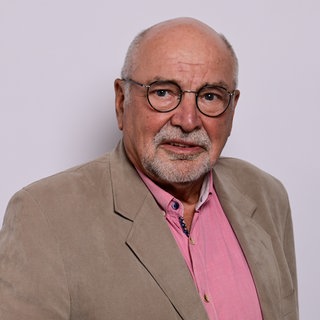 Kreuzfahrtschiff-Seelsorger Albert Matthias Neumann schaut direkt in die Kamera. Zu DDR-Zeiten war er Bassist in der Band von Nina Hagen. Nach seiner Ausreise aus der DDR war er fast 20 Jahre evangelischer Pastor im Hamburger Stadtteil Othmarschen und auch als Seelsorger auf Kreuzfahrtschiffen unterwegs. Darüber unterhalten wir uns mit ihm in SWR1 Leute.