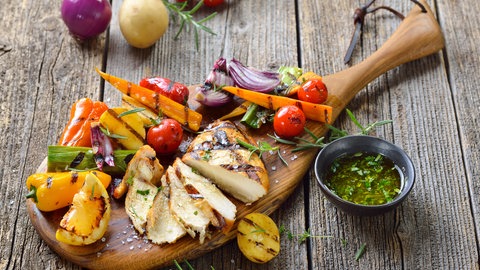 Grillgemüse und ein Hähnchensteak auf einem Holzbrett angerichtet | Nachhaltig grillen: So geht es richtig