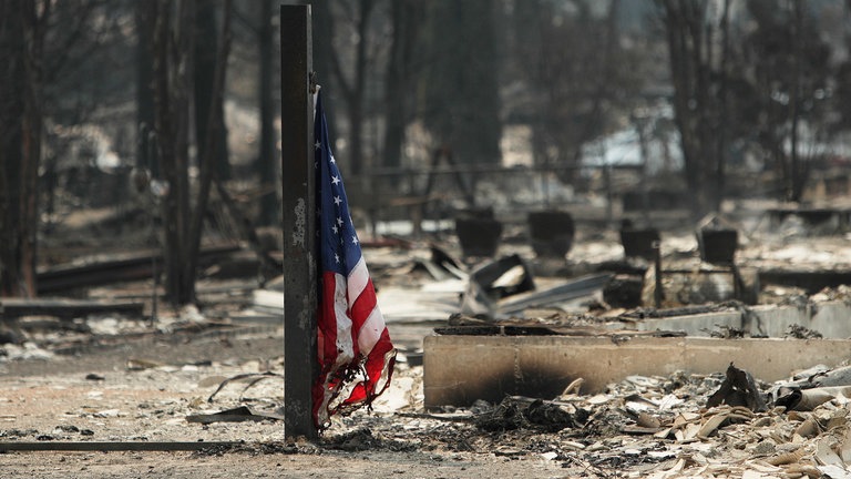 5. August: Eine amerikanische Flagge hängt vor einem abgebrannten Gebäude in einem Wohngebiet nach einem Waldbrand in Spokane, Washington. Bisher wurden bei den Feuern, bei denen die Polizei von Brandstiftung ausgeht, über 700 Gebäude zerstört, rund 64.000 Menschen evakuiert und rund 3.200 Hektar Wald vernichtet.