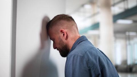 Ein Mann lehnt niedergeschlagen seinen Kopf an eine Wand.
