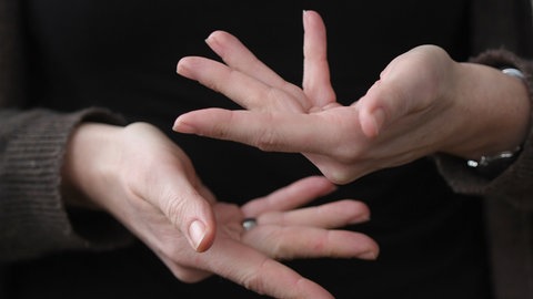 Eine Gebärdendolmetscherin zeigt mit ihren Fingern das Wort "beraten" in Gebärdensprache.