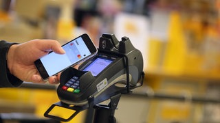 Ein Smartphone wird an den Bezahl-Terminal an der Kasse eines Supermarktes gehalten