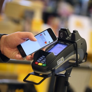 Ein Smartphone wird an den Bezahl-Terminal an der Kasse eines Supermarktes gehalten