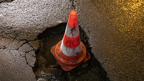 Ein orange-weiß gestreifter Verkehrs-Pylon steht in einem tiefen Schlagloch in einer Berliner Straße