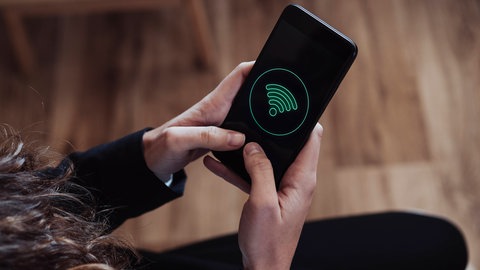 Eine Frau hat ein Smartphone mit WLAN-Logo auf dem Bildschirm in der Hand (Symbolbild)