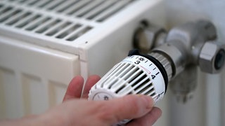 Eine Frau dreht an einem Heizungsthermostat.