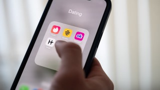 Eine Frau hält ein Smartphone, auf dem die Dating-Apps Tinder, Bumble, OkCupid und Hinge angezeigt werden.