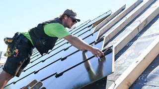 Handwerker arbeiten an einem Photovoltaik Dach. Die neuartige PV Anlage besteht aus Photovoltaik Modulen in Form von Dachplatten