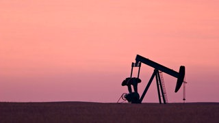 Eine Tiefpumpe zur Erdölförderung steht auf einem Feld im Abendrot.