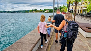 Eine junge Familie ist mit ihren beiden Kindern auf der Uferpromenade in Gardone Riviera, am Westufer des Gardasees, unterwegs.