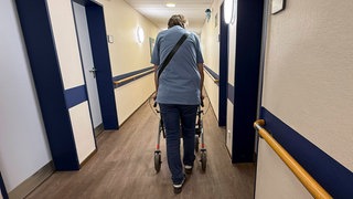 Symbolbild: Eine Bewohnerin geht mit ihrem Rollator im Flur des Matthias Claudius-Heims zu ihrem Zimmer.