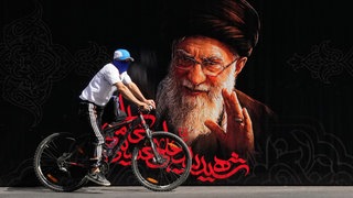 Ein Mann fährt mit dem Fahrrad an einem Porträt des getöteten iranischen Obersten Führers Ajatollah Ali Chamenei vorbei – kurz vor Beginn seiner mehrtägigen Trauerfeierlichkeiten