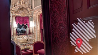 Eine Tür öffnet sich auf einen Balkon des klassizistischen Theaters in Baden-Baden und gibt den Blick auf Stühle, Balkon und Scheinwerfer frei.