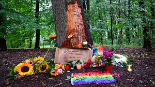 Blumen, Kerzen und die Botschaft „Wir gedenken aller Opfer und Überlebenden“ sind am Morgen an einem Baum mit beschädigter Rinde zu sehen, wo ein Fahrzeug am Rande des Christopher Street Day in eine Menschenmenge gefahren war.