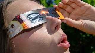 Eine junge Frau schaut durch eine Schutzbrille und betrachtet eine Sonnenfinsternis.