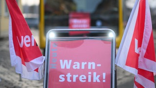 Symbolbild: Ein Schild "Warnstreik" steht vor einem Bus während des Warnstreiks im öffentlichen Nahverkehr.