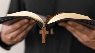 In einem von einem Priester geöffneten Buch liegt ein Rosenkranz. In Montabaur muss sich ein katholischer Geistlicher wegen sexuellen Missbrauchs verantworten.