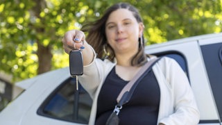 Eine Frau hält die Autoschlüssel vor ihrem neuen Elektroauto in der Hand. Sind gebrauchte Elektroautos eine gute Wahl?
