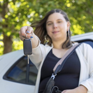 Eine Frau hält die Autoschlüssel vor ihrem neuen Elektroauto in der Hand. Sind gebrauchte Elektroautos eine gute Wahl?